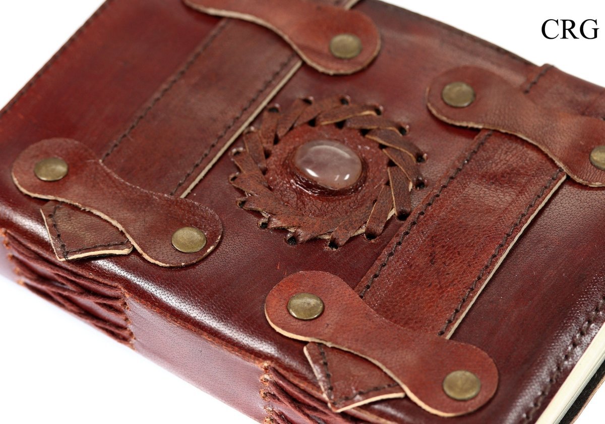 Angled close-up of rose quartz leather journal showing the stone accent, decorative straps and stitched spine