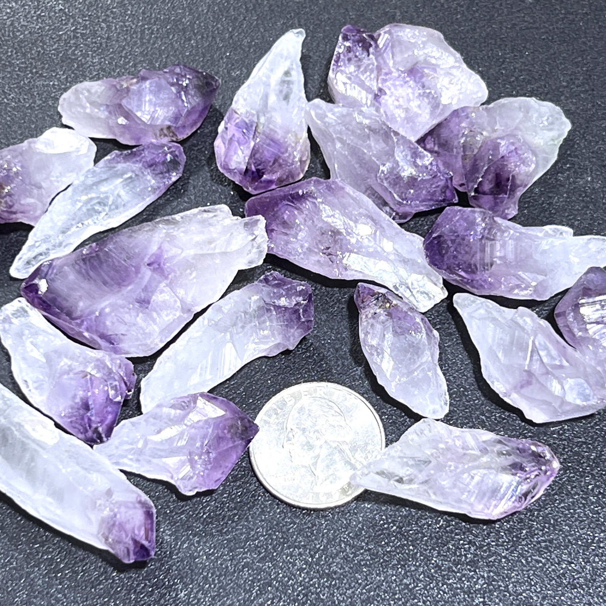 Purple and white rough amethyst crystal points beside a quarter for size comparison.

