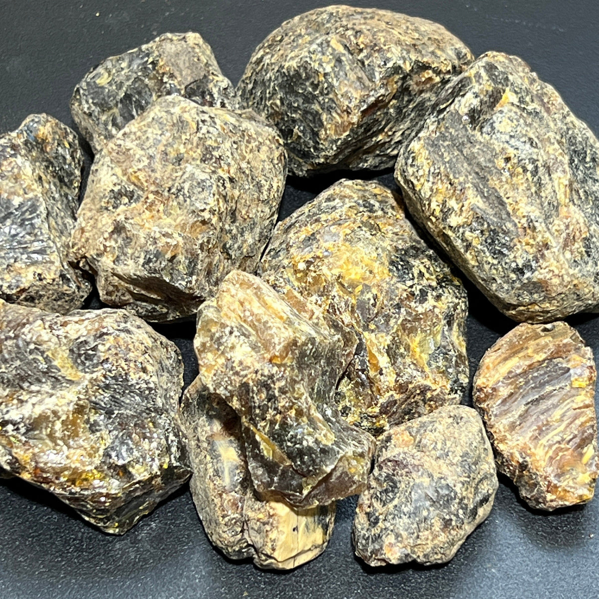  Group of rough black amber resin pieces with mottled dark and golden surfaces on a black background