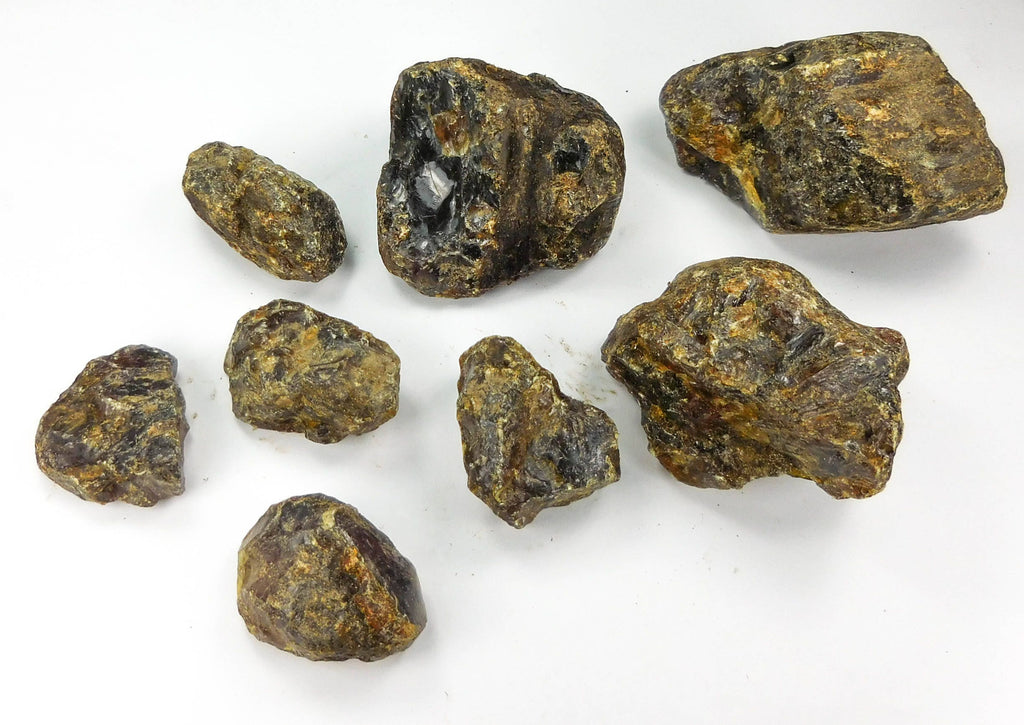 Eight assorted rough black amber pieces with dark brown surfaces and golden patches on a white background