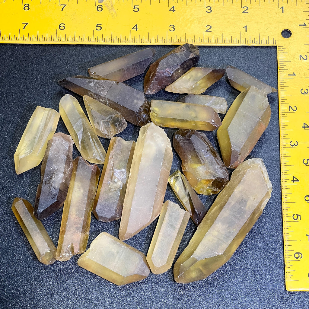 Mixed-size rough citrine crystal points on a dark surface framed by a yellow ruler for scale