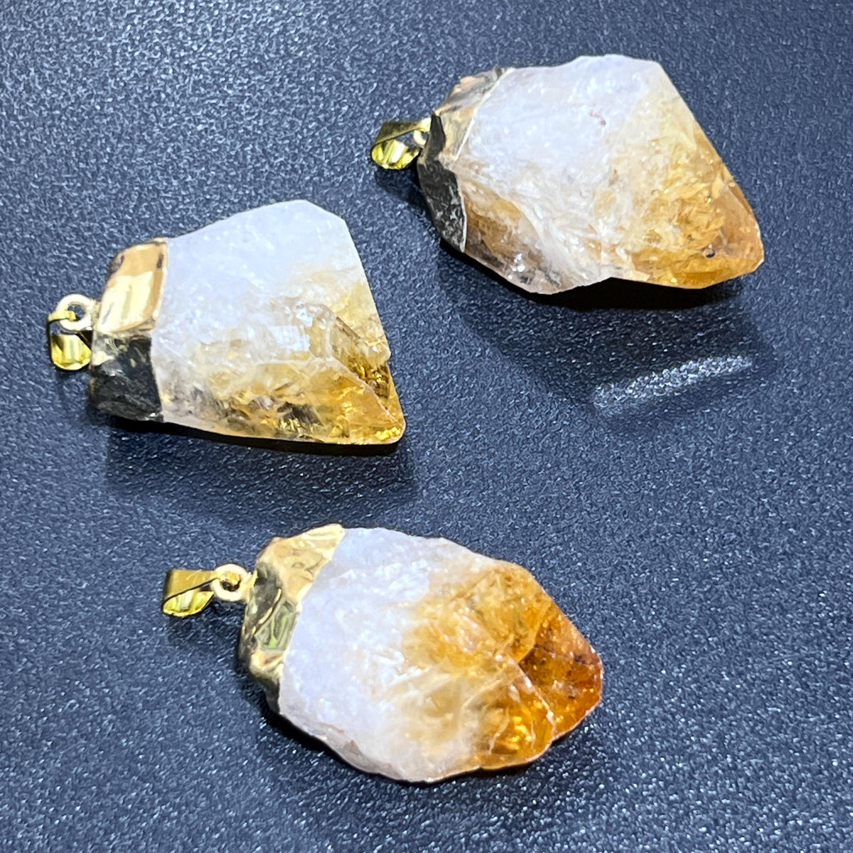 Three rough citrine point pendants made from treated amethyst with milky white bases, golden tips, and gold-plated fittings.