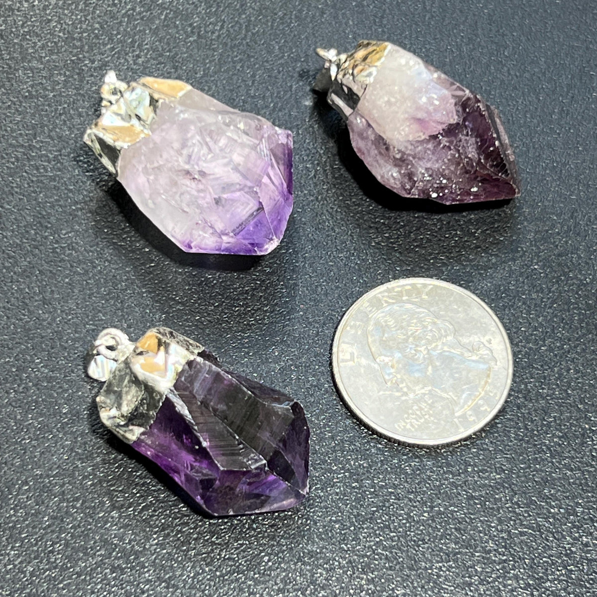Three amethyst crystal pendants on a dark surface with a coin for scale.
