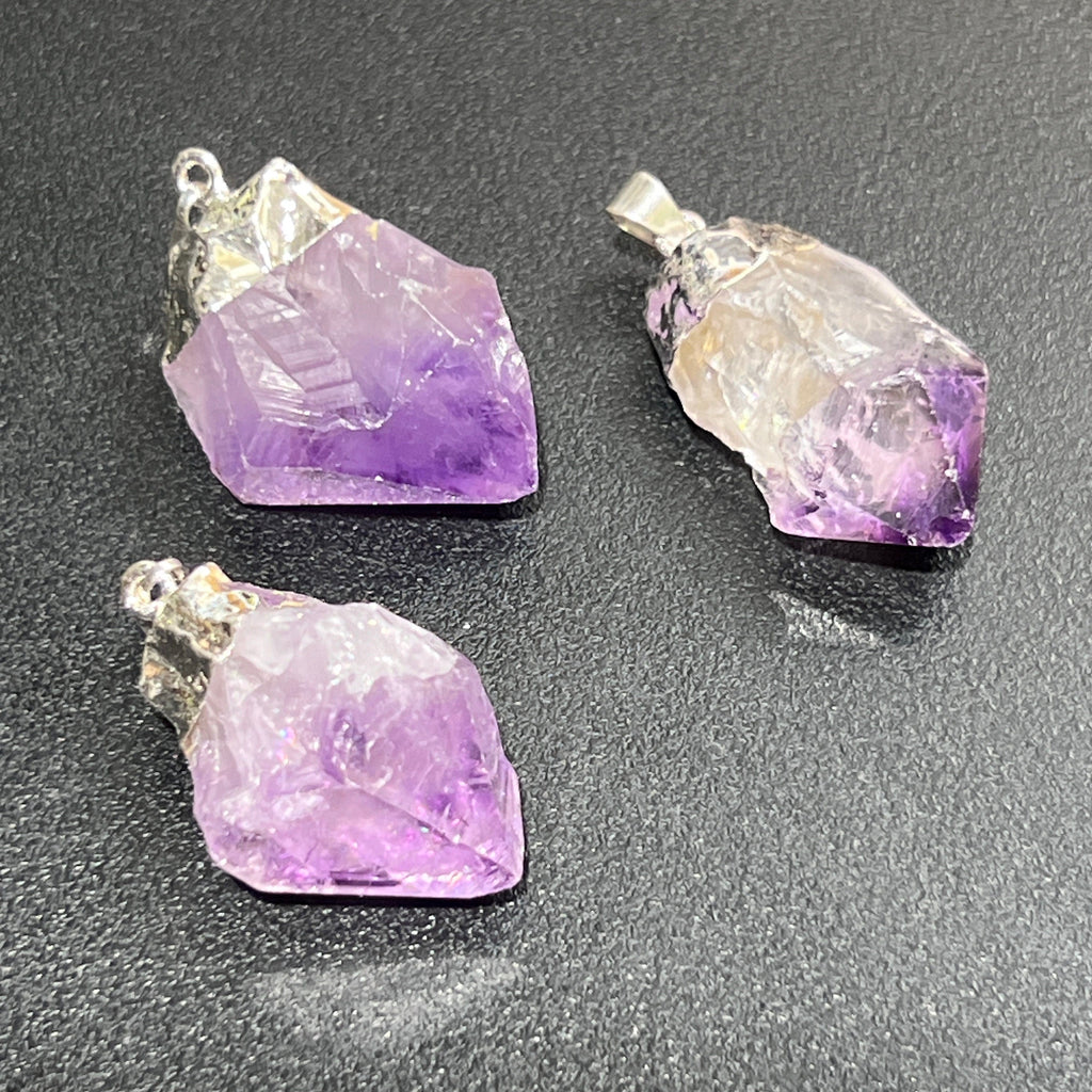 Three amethyst crystal pendants on a dark surface