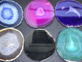Six polished round agate slices in blue, pink, purple, gray-brown, black and teal with varied bands and crystal centers