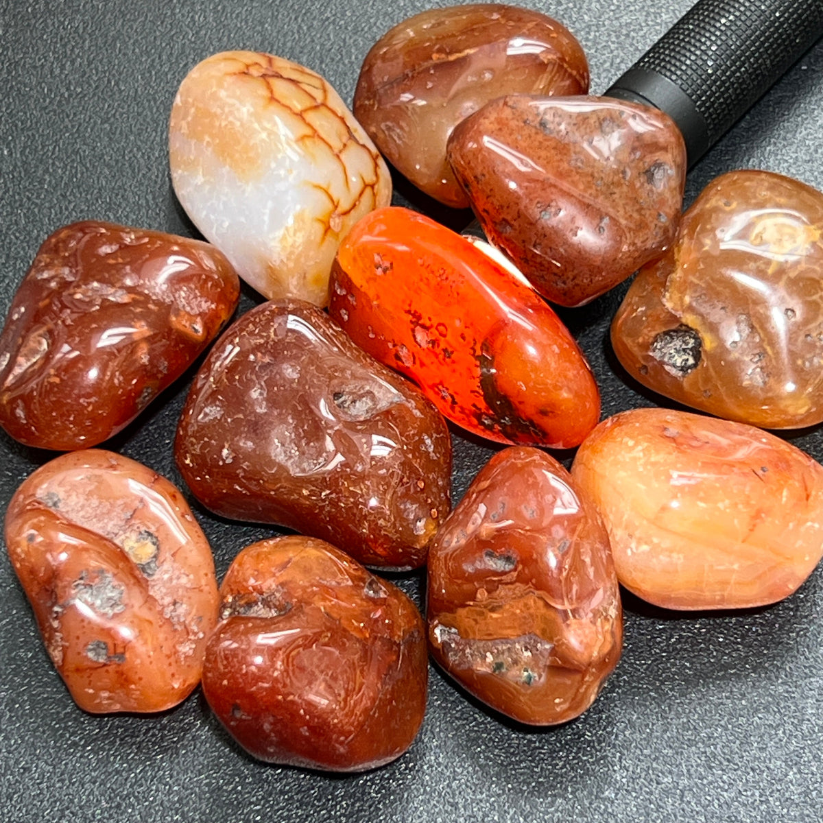 Close-up of rounded carnelian red agate stones with varied cream patches, dark inclusions and glossy surfaces