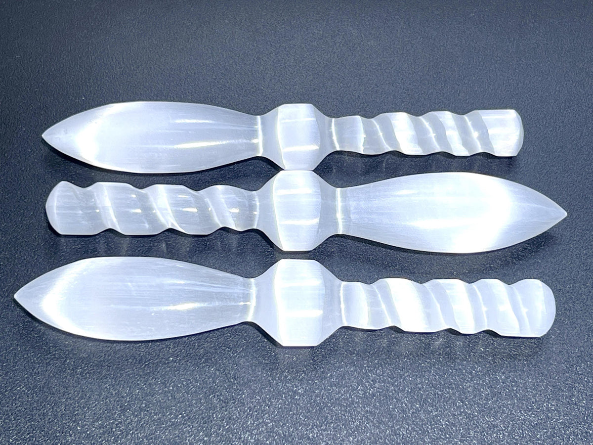 Overhead view of three satin spar crystal daggers showing pointed blades and spiral handles on a dark background
