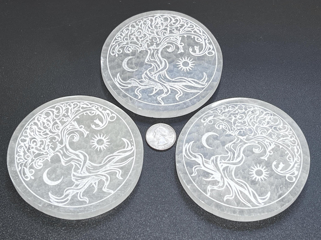 Three selenite Tree of Life plates with sun and moon engravings arranged around a quarter for size comparison.
