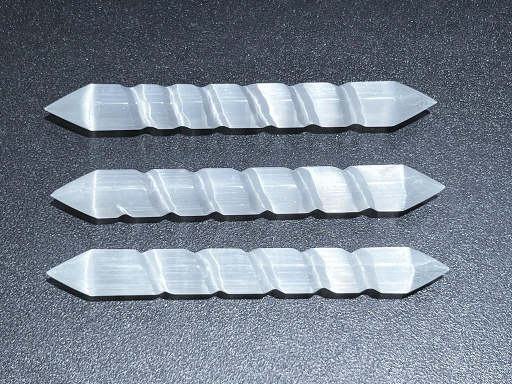 Three double-terminated selenite spiral wands arranged horizontally on a dark surface.