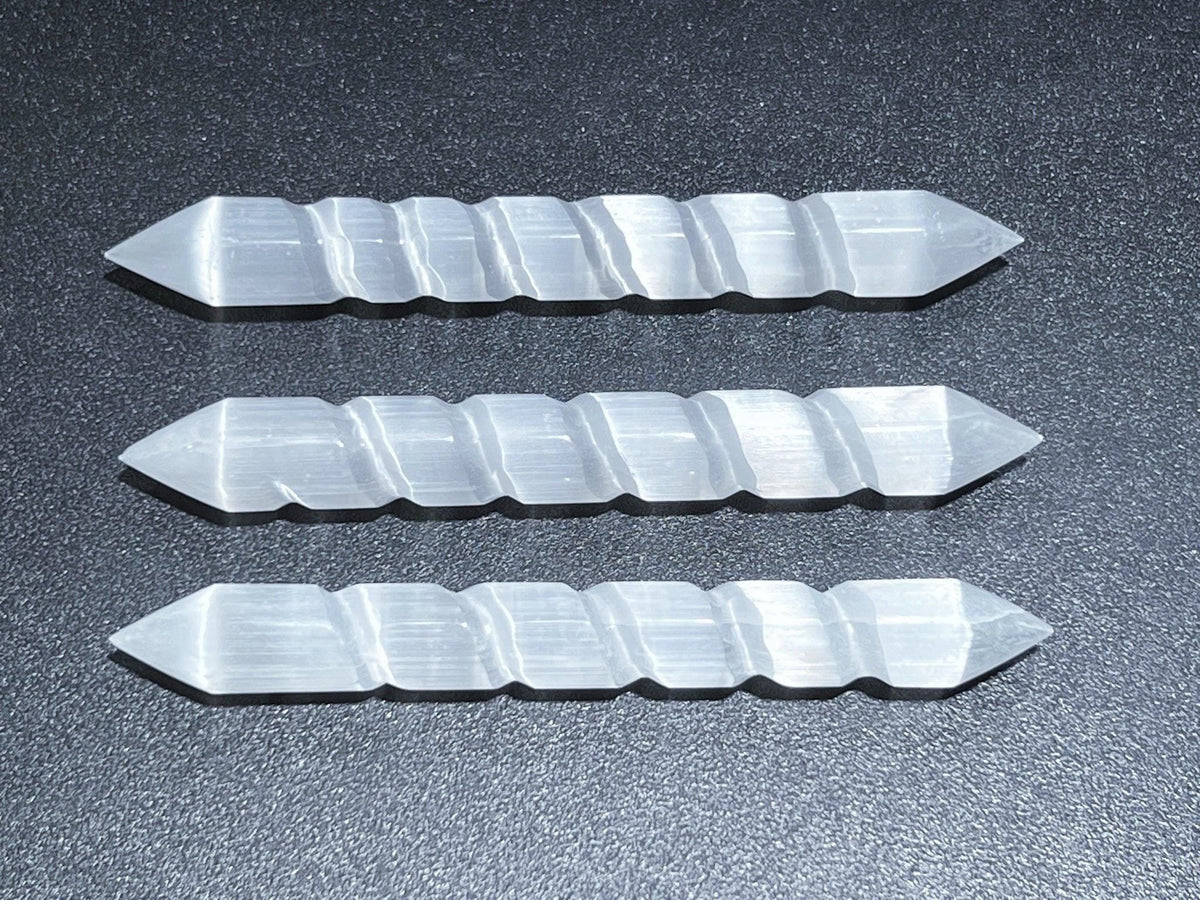 Three double-terminated selenite spiral wands arranged horizontally on a dark surface.