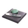 Black square shungite plate styled with a clear quartz point and a polished green stone on a white background.
