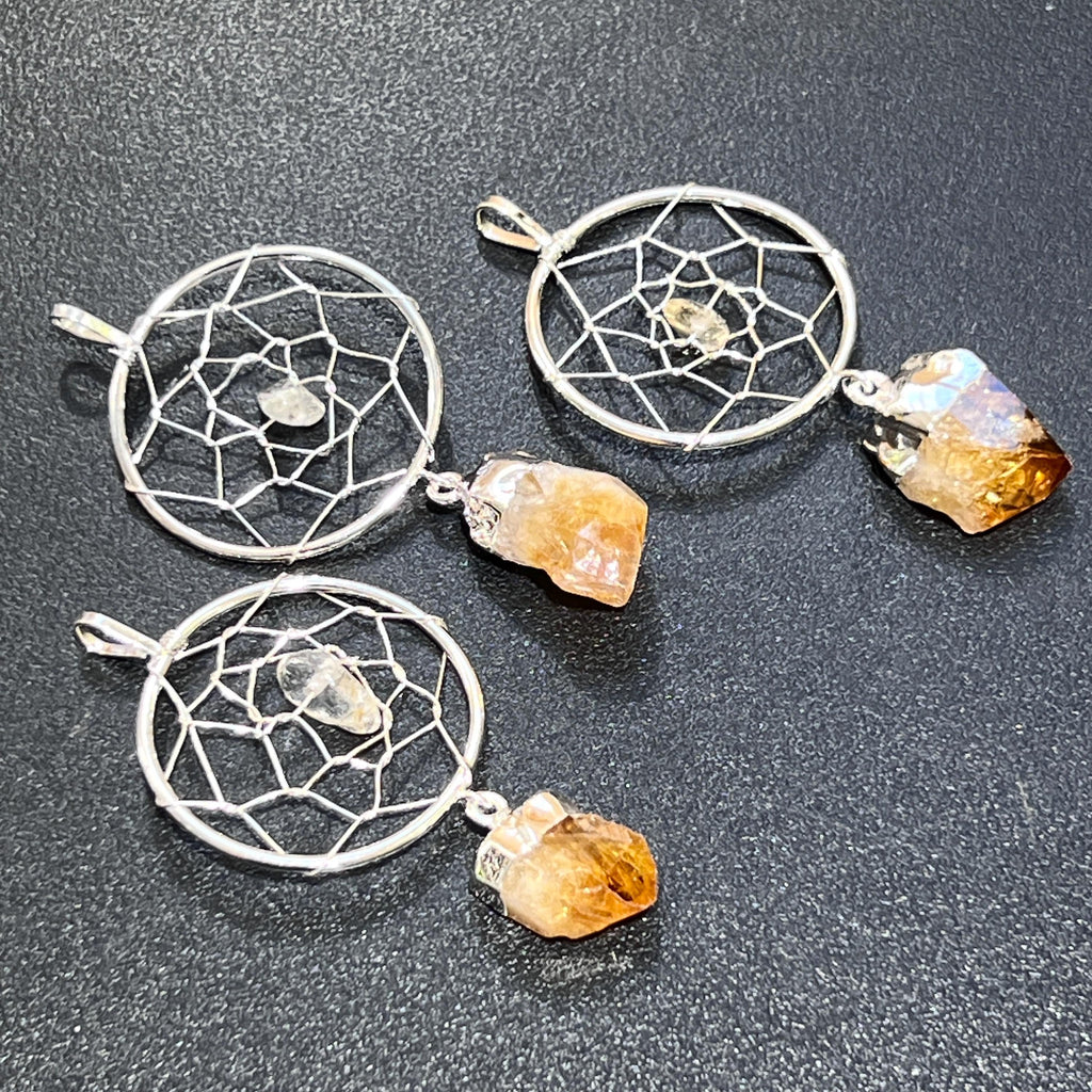 Three silver-plated dreamcatcher pendants with small center stones and yellow-to-amber citrine points on a dark surface.
