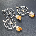 Three silver-plated dreamcatcher pendants with small center stones and yellow-to-amber citrine points on a dark surface.
