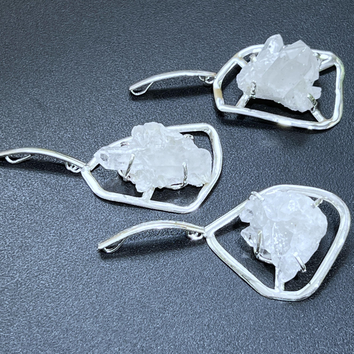 Three silver-plated open-frame pendants holding white quartz clusters, with elongated curved hanging bails.
