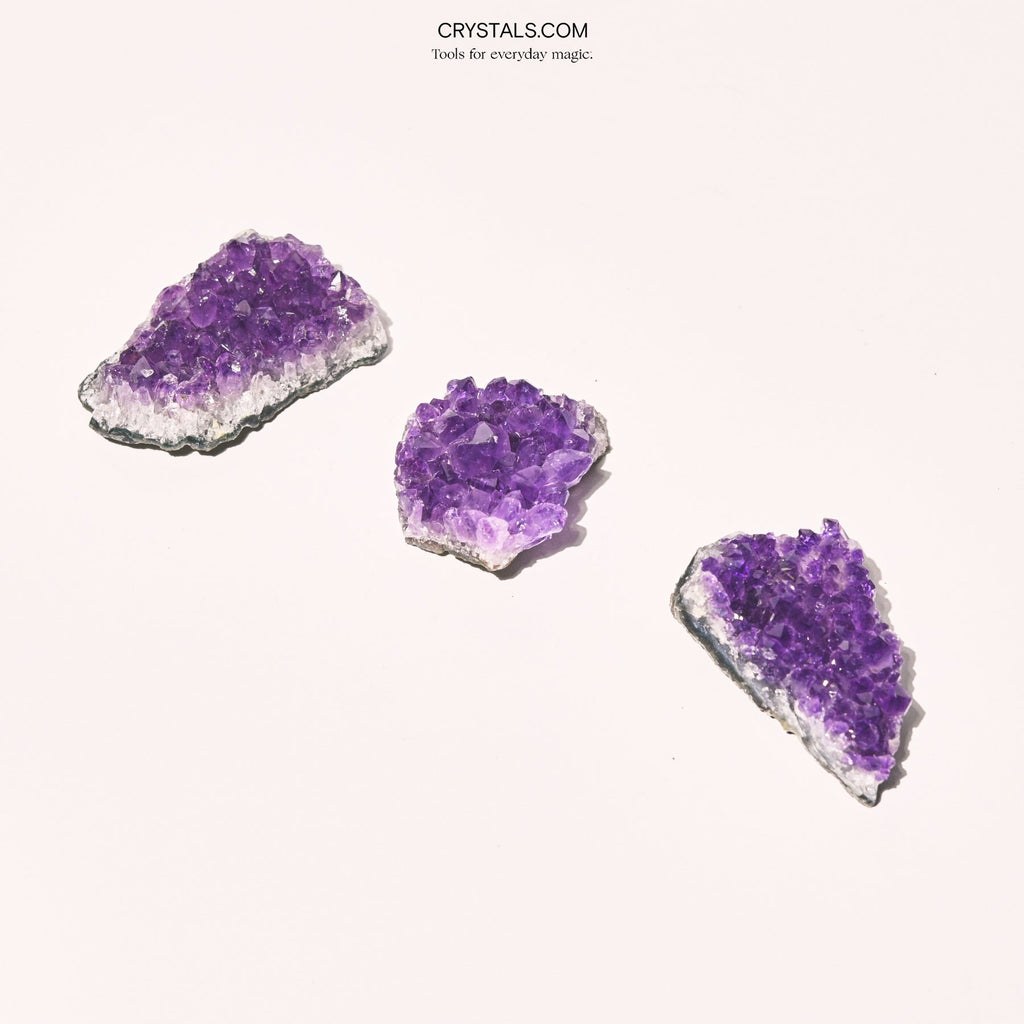 Three small purple amethyst clusters arranged diagonally on pale pink.
