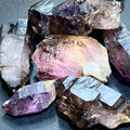 Raw smoky Shangaan amethyst points with purple, smoky brown, and pale translucent areas on a dark surface.