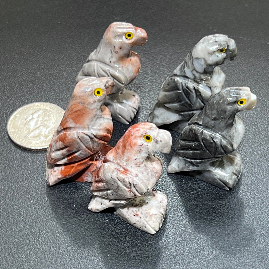Five miniature soapstone eagle carvings with curved beaks, carved wings and yellow eyes beside a coin