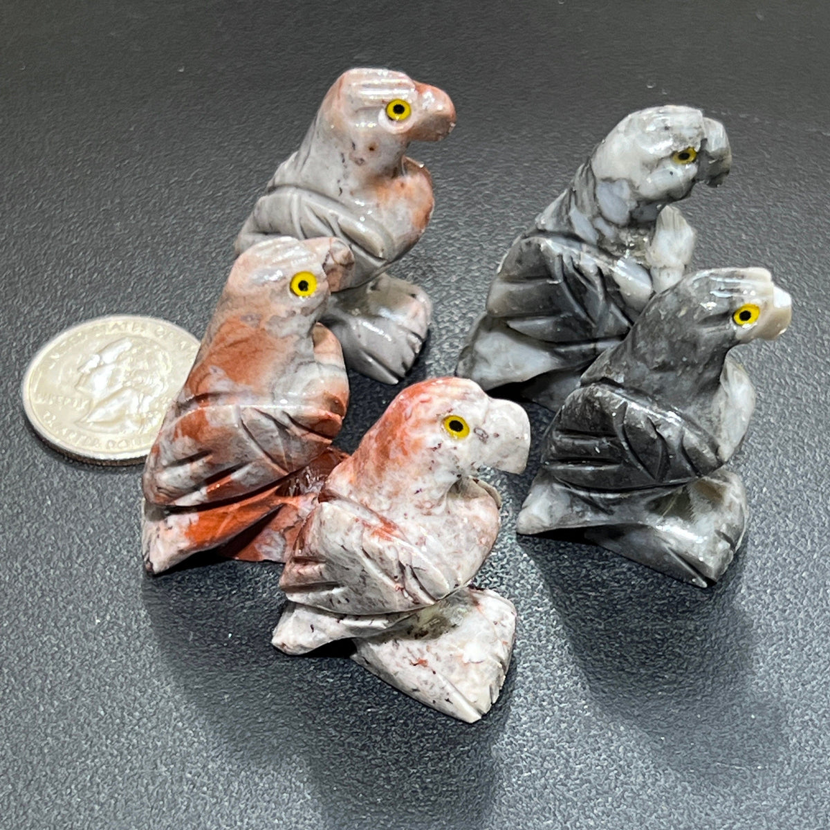 Five miniature soapstone eagle carvings with curved beaks, carved wings and yellow eyes beside a coin