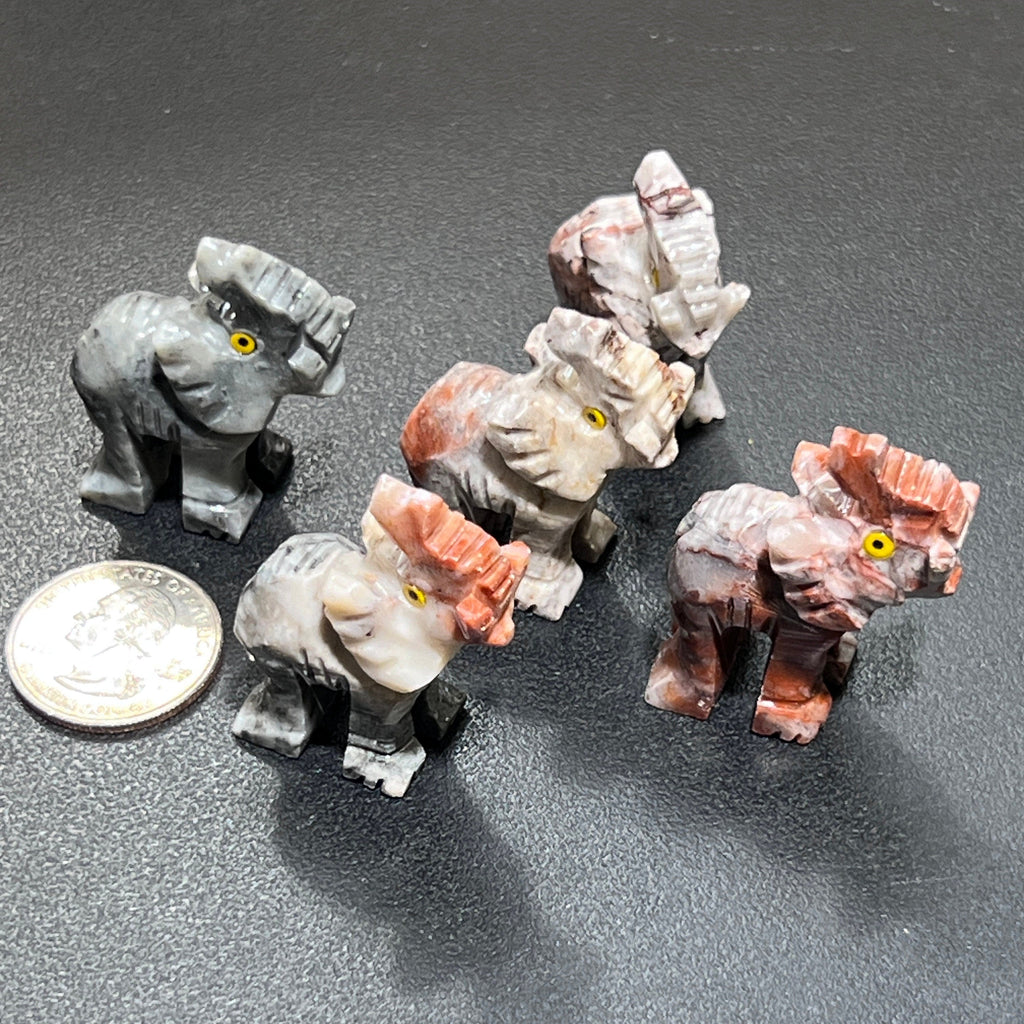 Five soapstone elephant figurines with raised trunks and marbled gray, cream and pink markings beside a coin