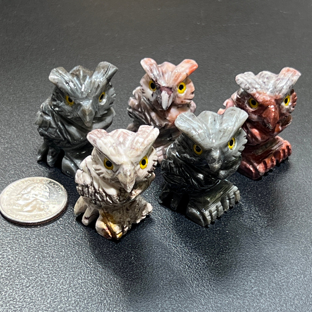 Five soapstone owl carvings with pointed ear tufts, carved feathers and bright yellow eyes beside a coin