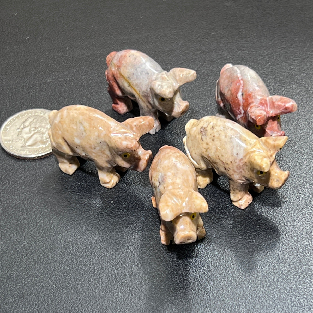  Five miniature soapstone pig figurines in cream, tan and pink with carved snouts beside a coin