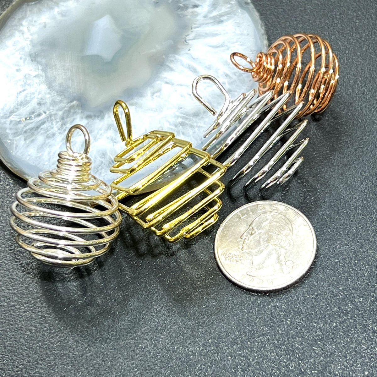 Assorted empty metal spiral cage pendants beside a quarter for scale on a dark surface