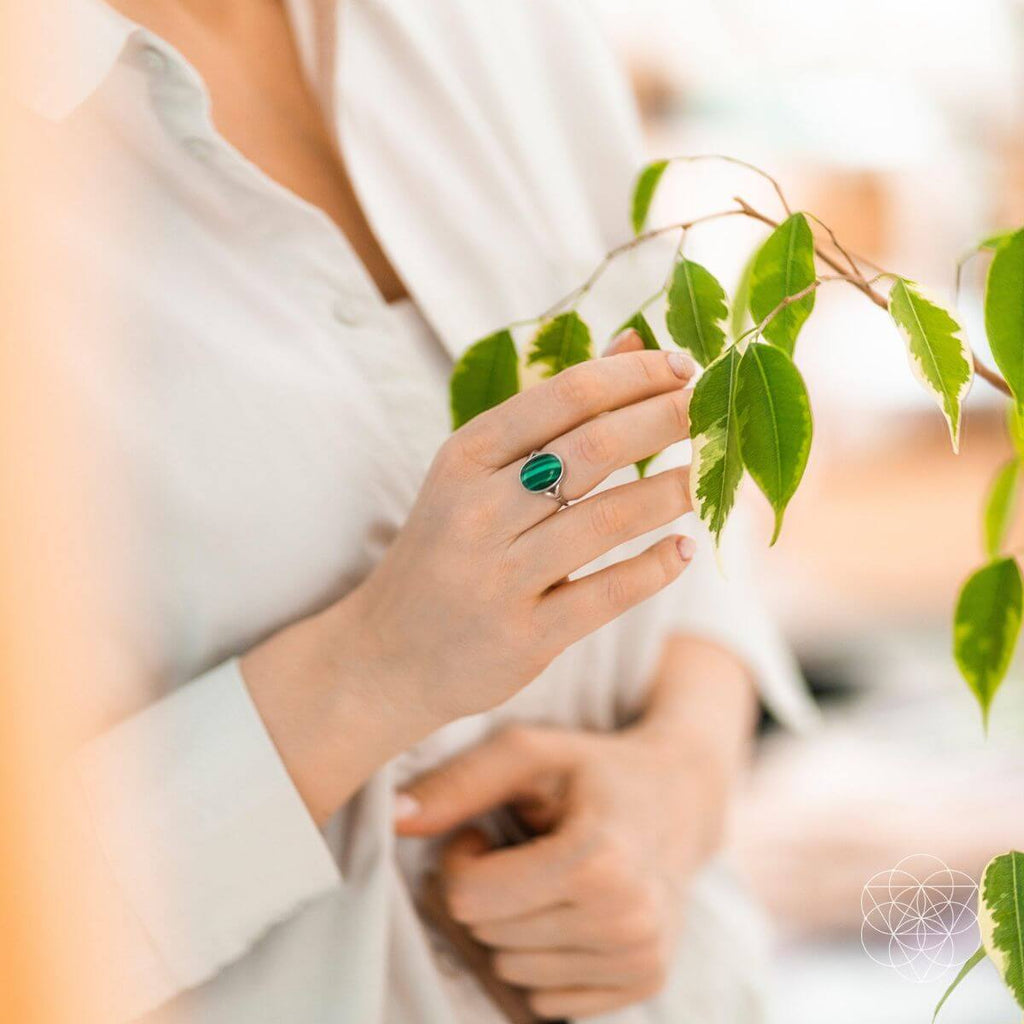 Model wearing an oval green malachite ring while touching a leafy branch.

