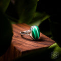 Oval green banded malachite ring with a silver-colored setting and openwork shoulders displayed on wood.
