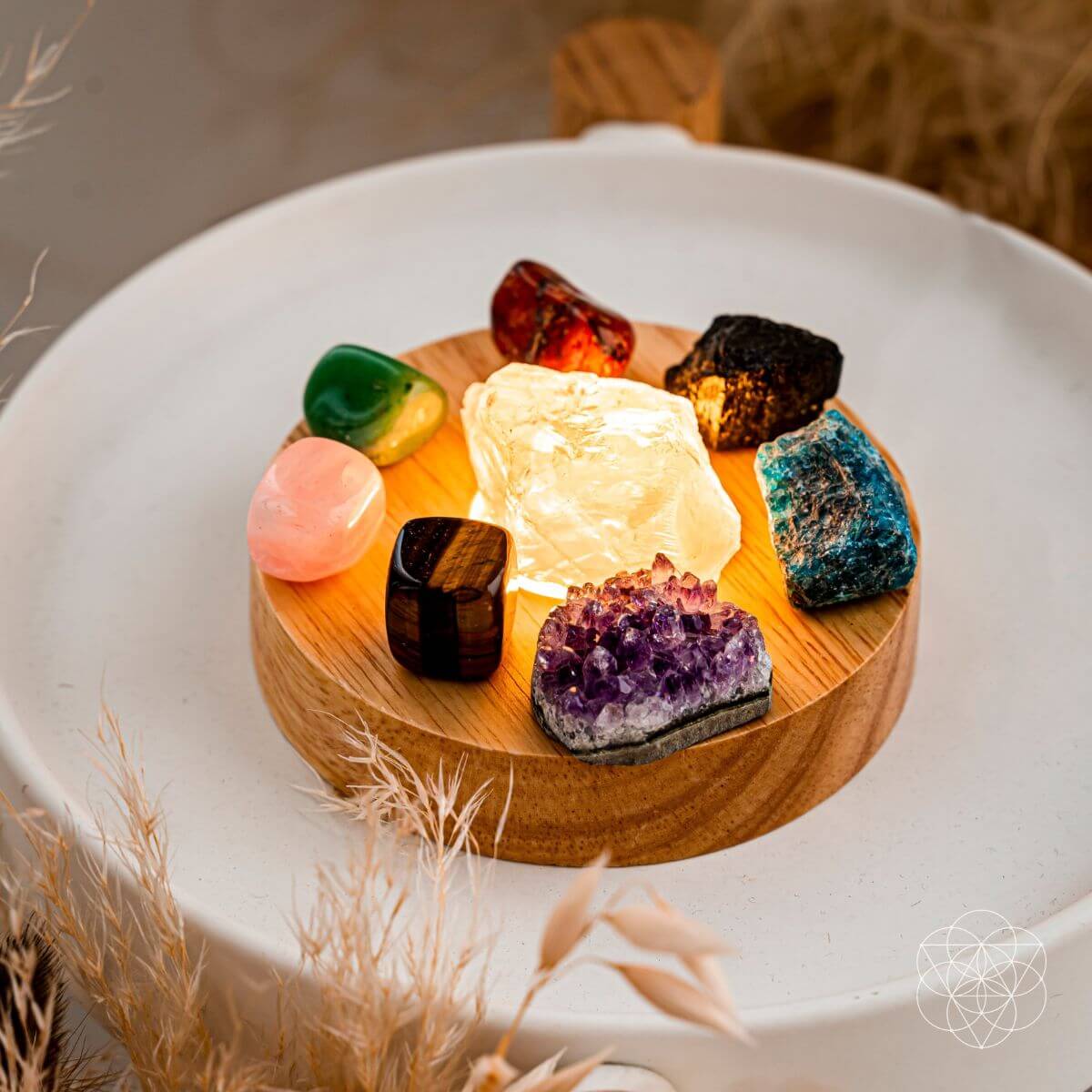 Overhead view of eight colorful stones surrounding glowing clear quartz on a wooden lamp base on a white tray.
