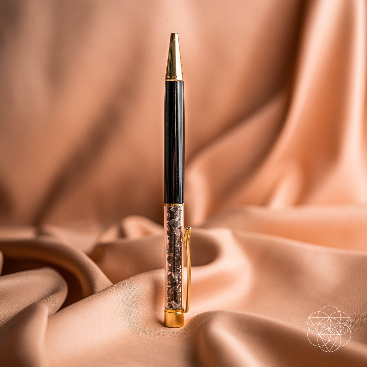 Black crystal-chip pen with gold-tone clip and tip standing upright on peach fabric.
