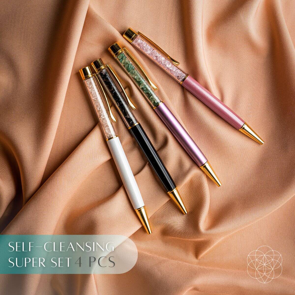 Four crystal-chip pens in white, black, lavender, and pink with gold-tone accents on peach fabric.