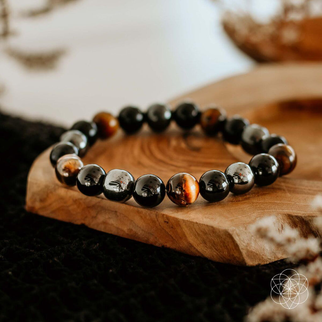 Tiger’s eye, black obsidian, and hematite beaded bracelet displayed on a wooden slice.