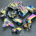 Small titanium aura quartz clusters and rough points with rainbow-colored crystal faces on a dark textured surface.
