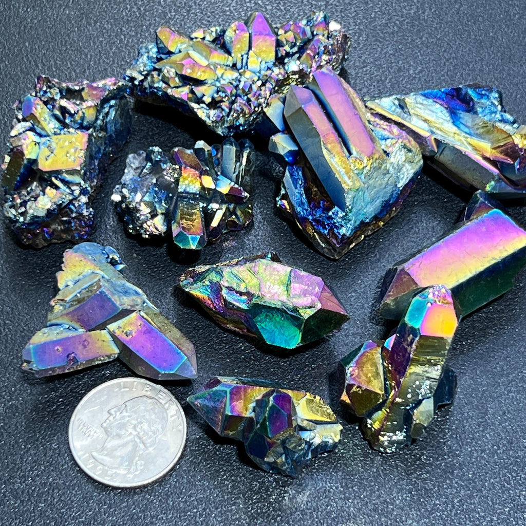 Small rainbow-finished titanium aura quartz clusters and rough points beside a quarter for size comparison.
