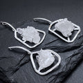 Three white quartz cluster pendants in silver-plated open frames with elongated bails arranged on dark slate.
