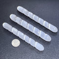 Three white satin spar selenite spiral wands with rounded ends beside a quarter on a dark surface.
