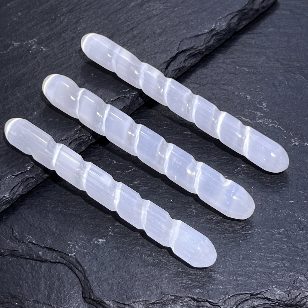 Three rounded white satin spar spiral wands arranged diagonally across layered dark slate.

