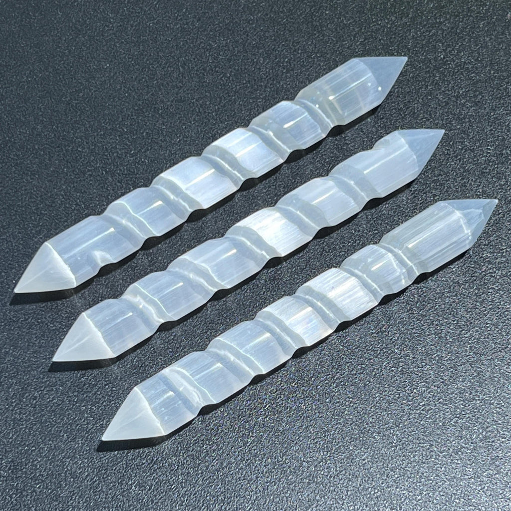 Three white selenite wands showing spiral-carved grooves and pointed ends on a dark textured background.